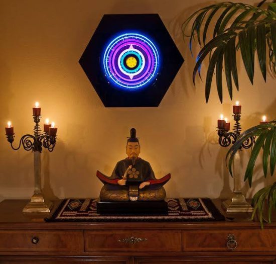 art installation in private home with Lumonics light sculpture on wall with seated Buddha on wood table
